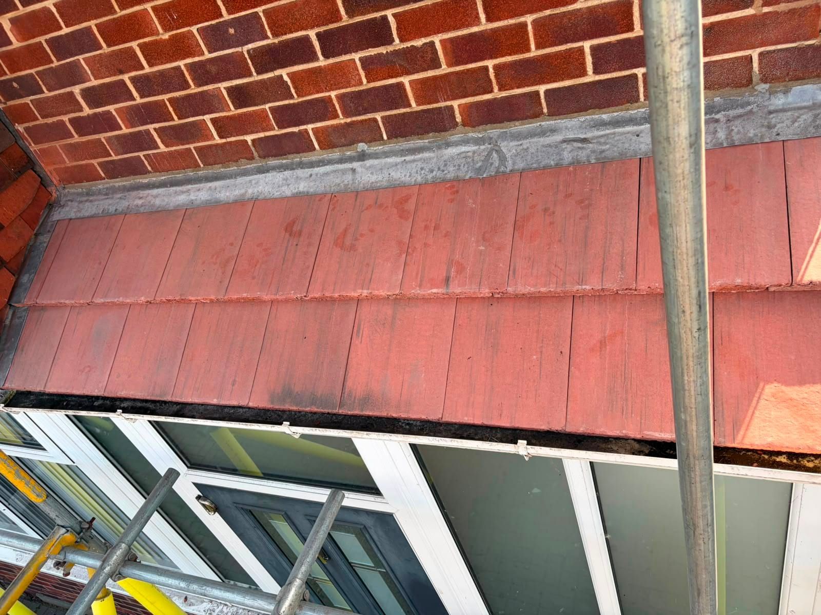 A small red tiled roof over a bay window, with lead flashing where it meets the brick wall above