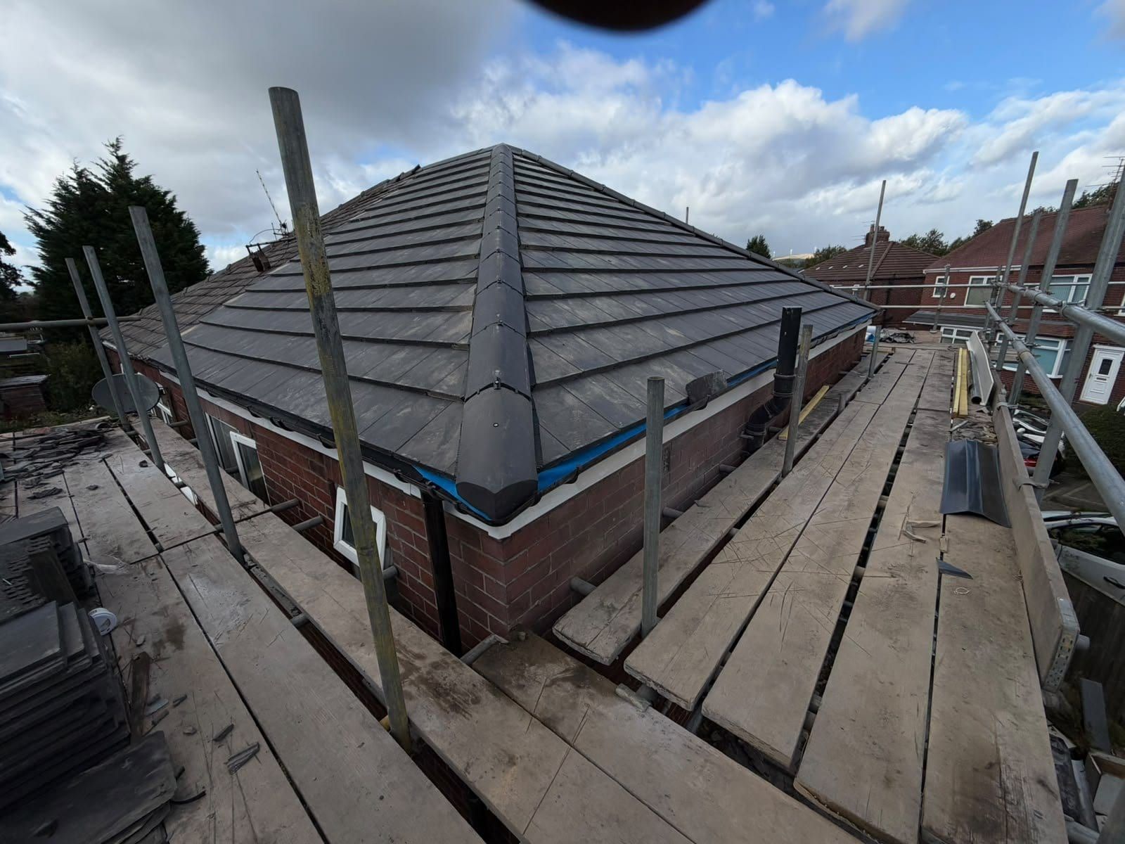 A new grey tiled hip roof on a bungalow seen from the scaffold boards, with the scaffold poles still up