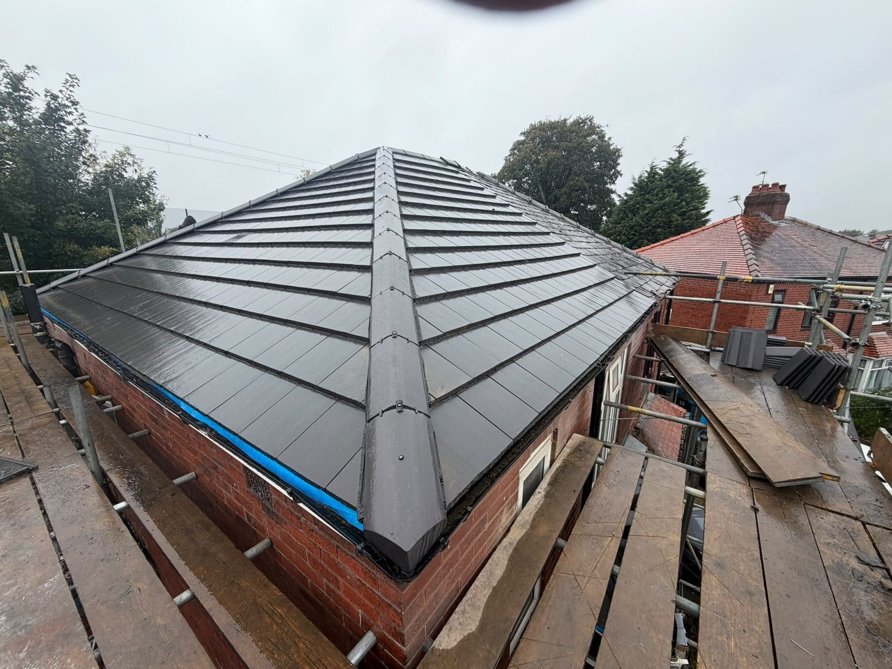 A bungalow with a new dark grey tiled hip roof and dry fixed ridge, with scaffolding round it