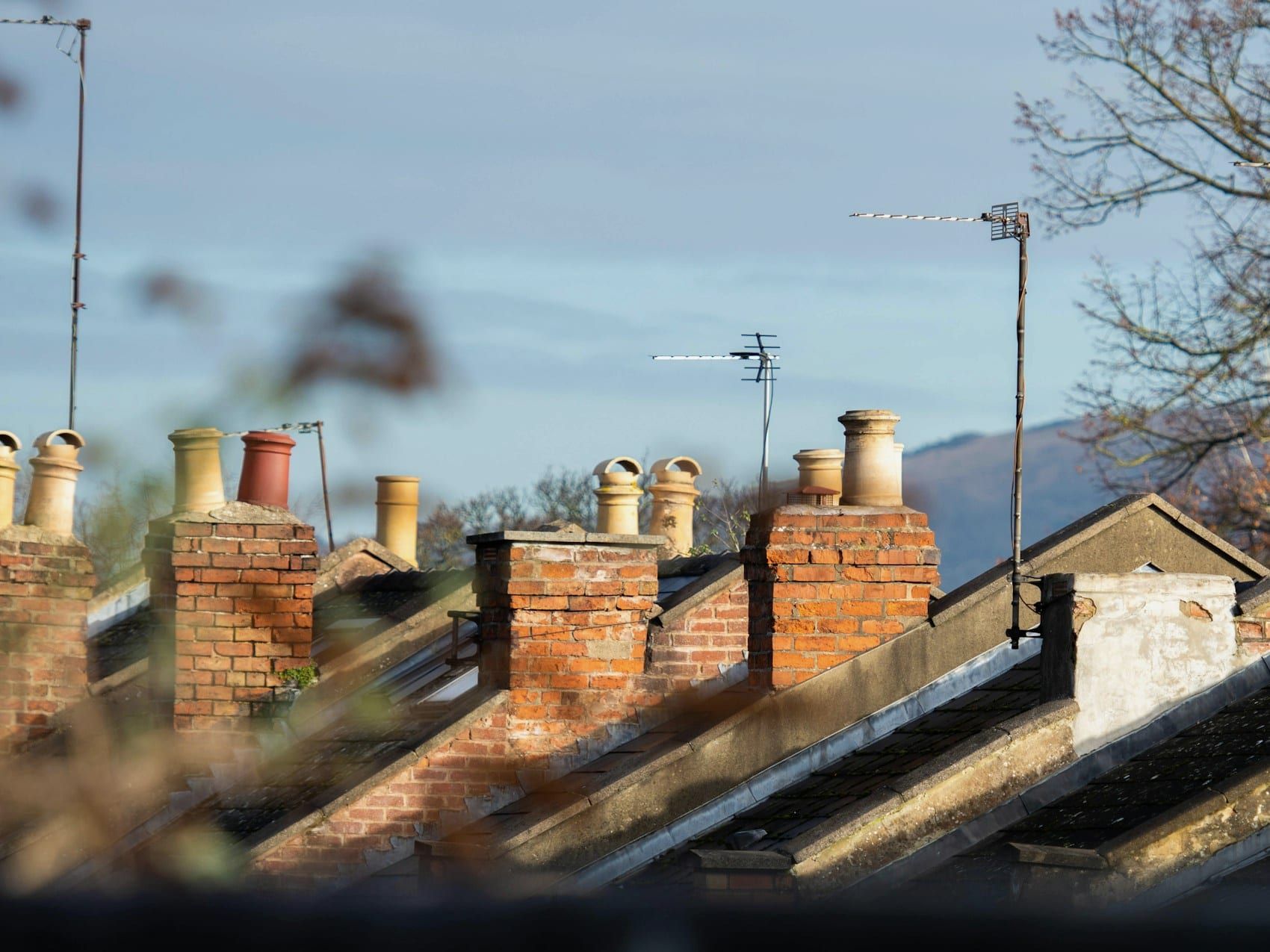 A row of terraced house roofs with brick chimney stacks and clay chimney pots against the sky