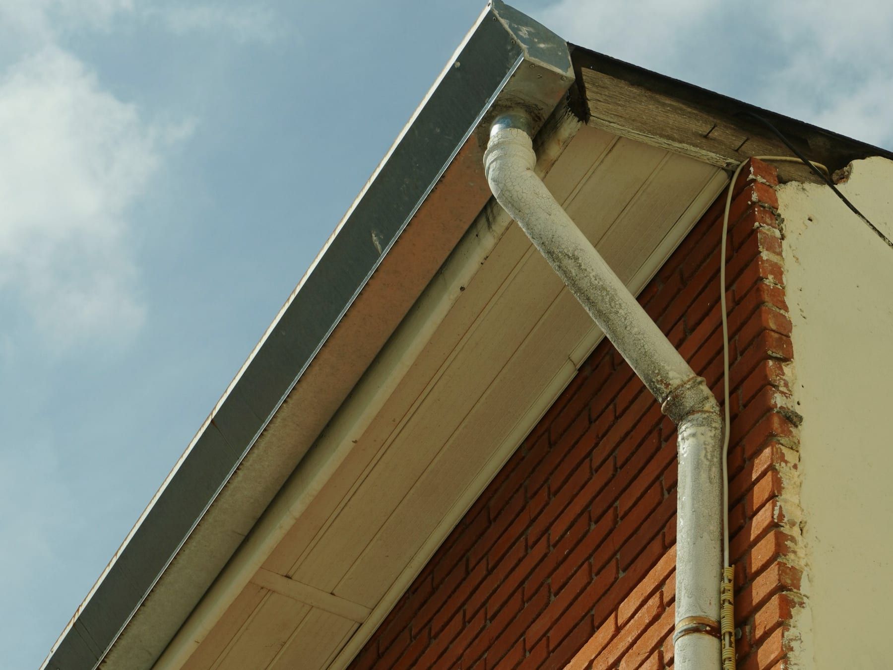 A white gutter and downpipe running down the corner of a red brick house under a white soffit