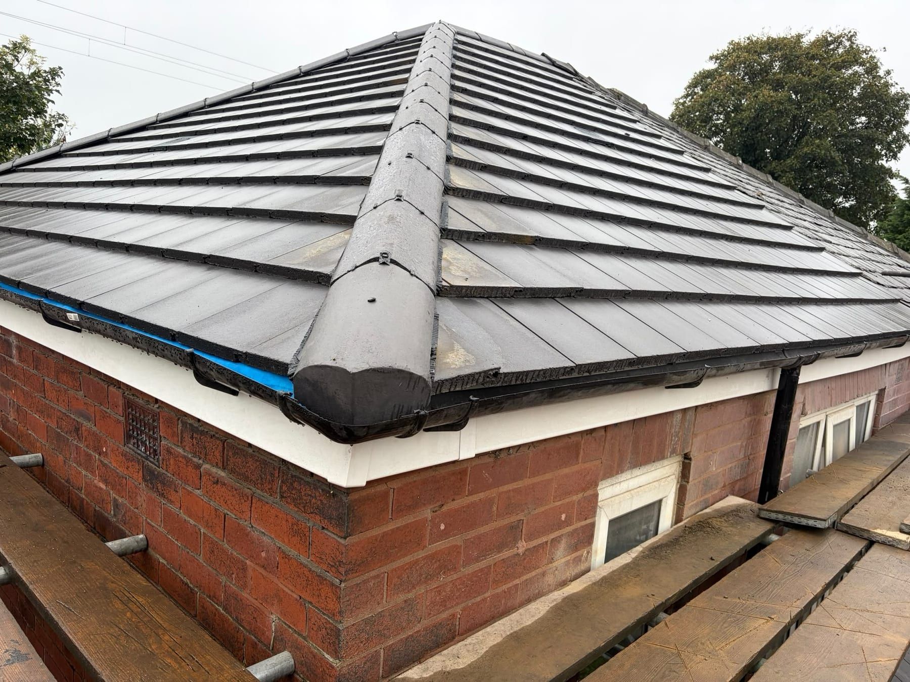 The corner of a new tiled hip roof, with a dry fixed hip ridge and a white fascia board below