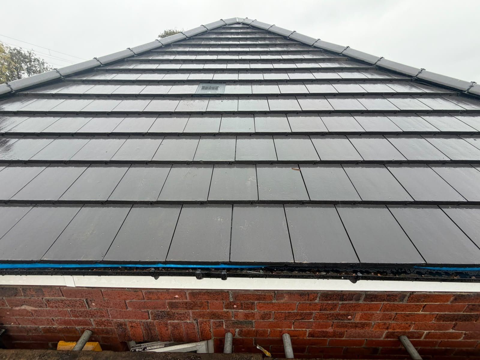 A finished slope of new dark grey interlocking roof tiles on a bungalow, seen from the scaffold