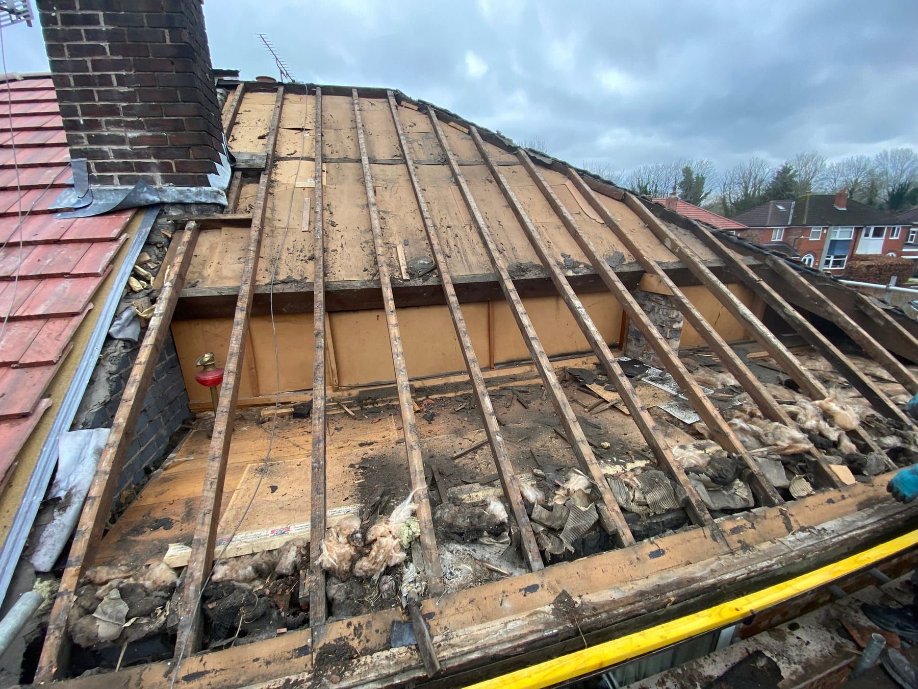 An old roof stripped back to the rafters next to the chimney stack, with the old boarding and debris showing
